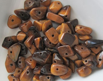 May include: A collection of tumbled tiger's eye beads in various shapes and sizes. The beads are primarily shades of brown and gold, with a polished, glossy finish. Each bead has a small hole for stringing.