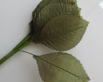 May include: A collection of olive green fabric leaves with green wire stems. The leaves are grouped together, with some single leaves extending out. The leaves have a textured look, and the stems are bound with green tape.