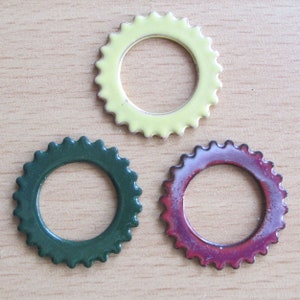 May include: Three colorful, circular metal rings with a scalloped edge. One is pale yellow, another is dark green, and the third is a reddish-purple color. The rings are arranged on a light brown wooden surface.
