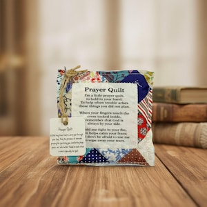 May include: A small, colorful prayer quilt with a tag. The quilt is made of patchwork fabric in various patterns and colors. The tag reads "Prayer Quilt" and includes a poem. The quilt is designed to be held and offers comfort.