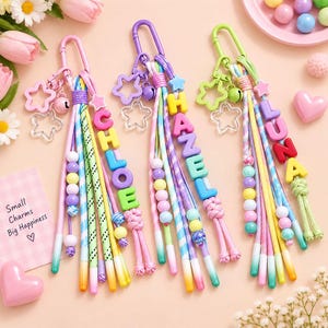 May include: Three colorful keychains featuring pastel cord tassels, star-shaped charms, and letter beads spelling CHLOE, HAZEL, and LUNA. Each keychain includes a metal clasp, small round bells, and a variety of beads in pink, yellow, blue, and green.