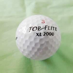 May include: A white golf ball with the text "TOP-FLITE XL 2000" and the number "3" printed on it.
