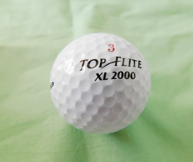 May include: A white golf ball with the text "TOP-FLITE XL 2000" and the number "3" printed on it.
