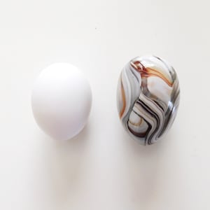 May include: A white egg and a marble with brown and gray swirling patterns.
