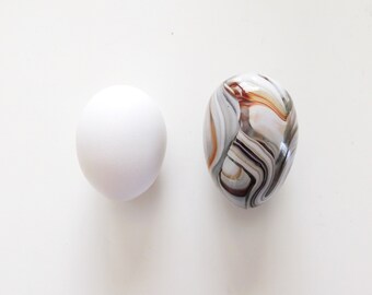 May include: A white egg and a marble with brown and gray swirling patterns.