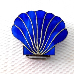 May include: A blue stained glass seashell nightlight with silver accents. The seashell is shaped like a clam with a textured surface.