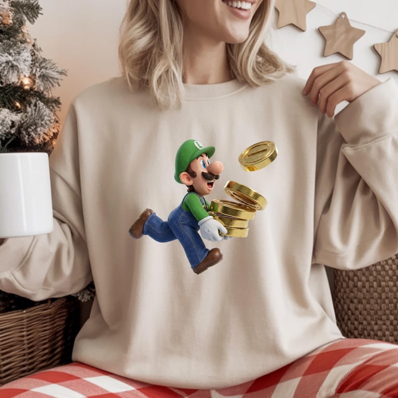 May include: Beige sweatshirt featuring a graphic of Luigi from the Super Mario Bros. series, running with a stack of gold coins. Luigi is wearing a green hat, green shirt, blue overalls, and white gloves. The sweatshirt is a neutral color.