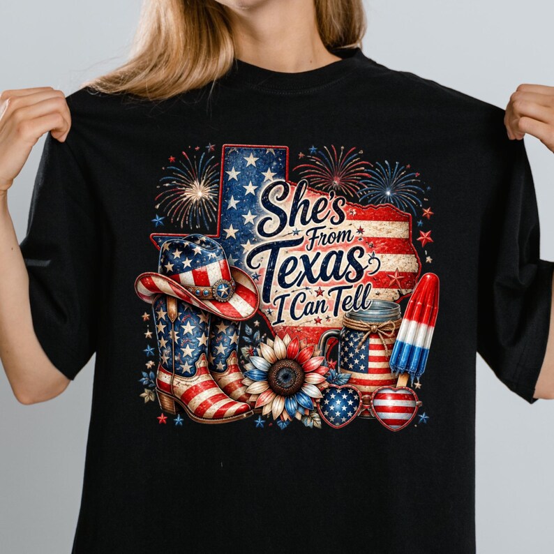 Pode incluir: Uma t-shirt preta com um gr&aacute;fico do estado do Texas com padr&otilde;es da bandeira americana, fogo de artif&iacute;cio, um chap&eacute;u de cowboy, botas, um girassol, um frasco, &oacute;culos em forma de cora&ccedil;&atilde;o e um gelado, com o texto She's From Texas I Can Tell.
