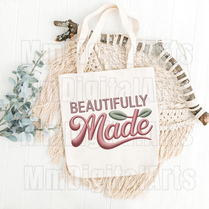 May include: A white tote bag with the words "BEAUTIFULLY Made" in a script font. The text is in a mauve color with a leaf design. The bag is on a white surface with decorative elements.