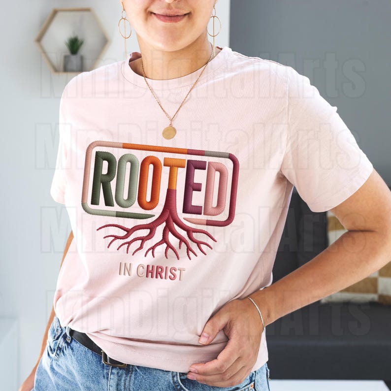 May include: A light pink t-shirt with the word "ROOTED" in a rectangular frame, featuring a tree root design. The text "IN CHRIST" is below the graphic. The shirt is a crew neck style.