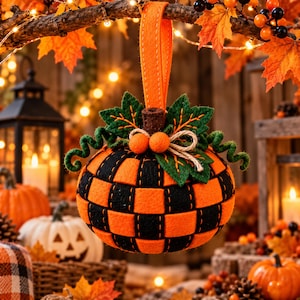 May include: A hanging pumpkin ornament crafted from woven orange and black felt strips. The top features green felt leaves, two small orange felt balls, a brown stem, and a jute twine bow, all suspended by an orange felt loop strap.