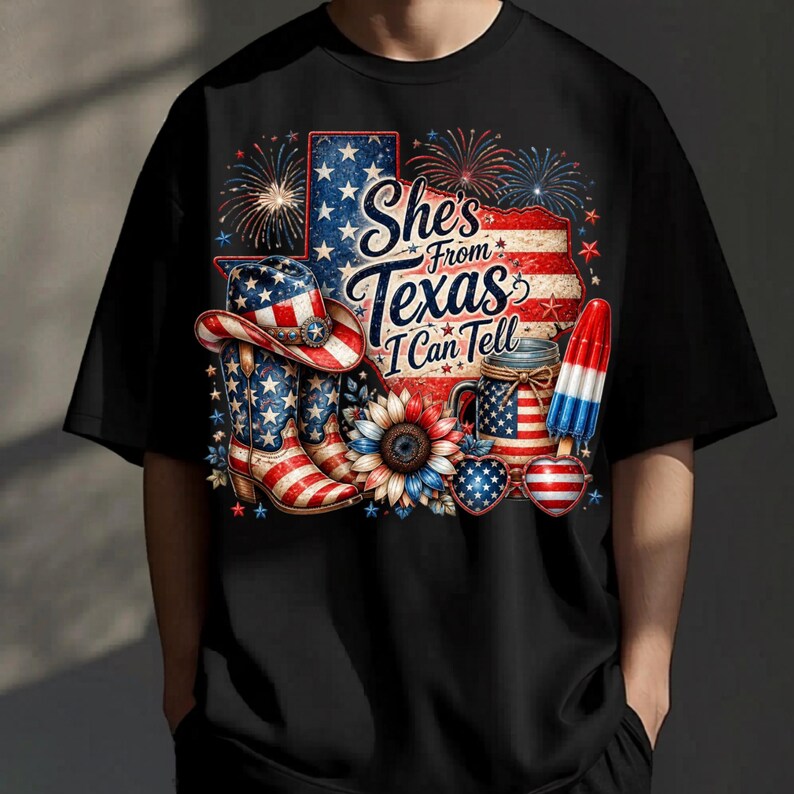 Pode incluir: Uma t-shirt preta com um gr&aacute;fico de uma bandeira em forma do Texas, um chap&eacute;u de cowboy, botas, um girassol, um frasco e um gelado, tudo com padr&otilde;es da bandeira americana. O texto "She's From Texas I Can Tell" est&aacute; rodeado por fogo de artif&iacute;cio.