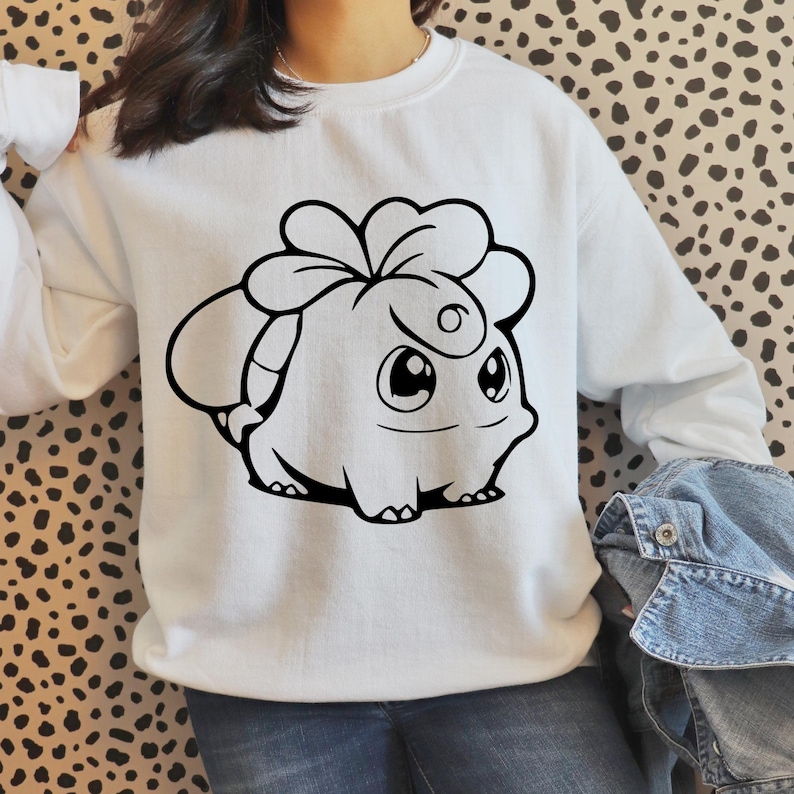May include: White sweatshirt featuring a black cartoon character design. The graphic is a stylized creature with large eyes, a smiling mouth, and a unique head shape. The sweatshirt has long sleeves and a crew neck.