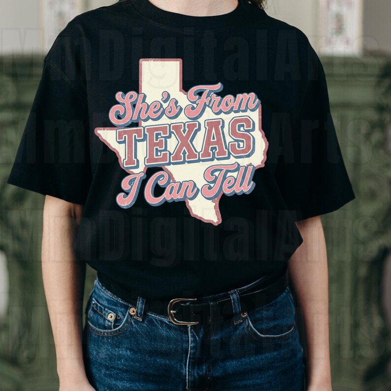 May include: Black t-shirt with a cream-coloured Texas state graphic and the text "She's From TEXAS I Can Tell" in pink and blue. The shirt is made of a soft material and has short sleeves.