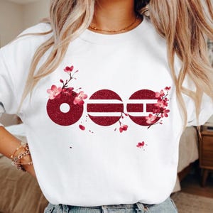 Puede incluir: Sudadera blanca con un diseño burdeos de tres círculos con rayas horizontales, acentuado con flores rosas. El diseño está centrado en la parte delantera. La sudadera está hecha de un material suave.