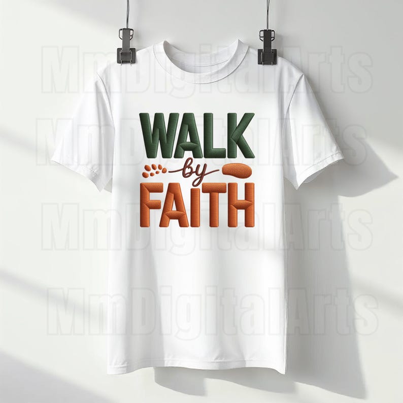 May include: White t-shirt with the text "WALK by FAITH" in green and orange block letters. The shirt is hanging on a hanger against a white background. The design includes a stylized footprint.