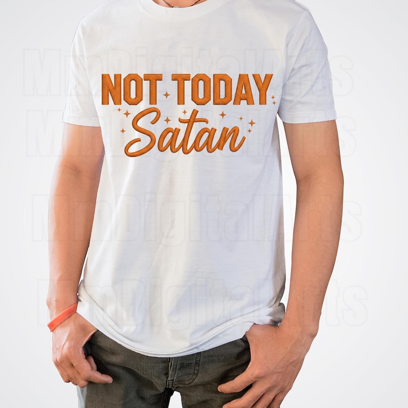 May include: White t-shirt with the phrase "NOT TODAY Satan" in orange block letters and script. The shirt has a crew neck and short sleeves. The text is surrounded by small starbursts.