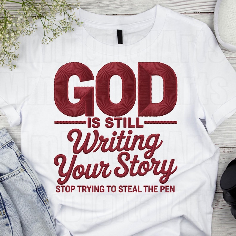 May include: White t-shirt with the embroidered text "GOD IS STILL Writing Your Story STOP TRYING TO STEAL THE PEN" in a burgundy color. The shirt is made of a soft material and is suitable for casual wear.