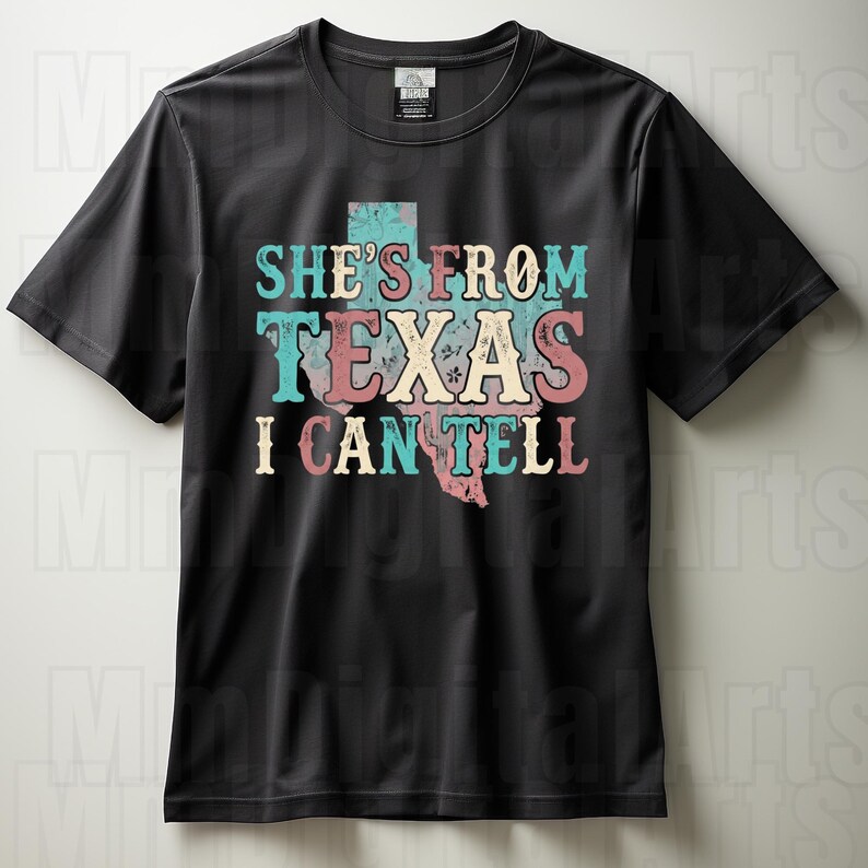 May include: Black t-shirt featuring the text "SHE'S FROM TEXAS I CAN TELL" in turquoise, pink, and cream. The design includes a map of Texas. The shirt has a crew neck and short sleeves.