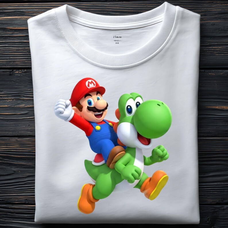 May include: White t-shirt featuring a colorful graphic of Mario riding Yoshi. Mario is wearing a red hat, blue overalls, and a mustache. Yoshi is green with a white belly and orange shoes. The shirt is folded on a dark wood surface.
