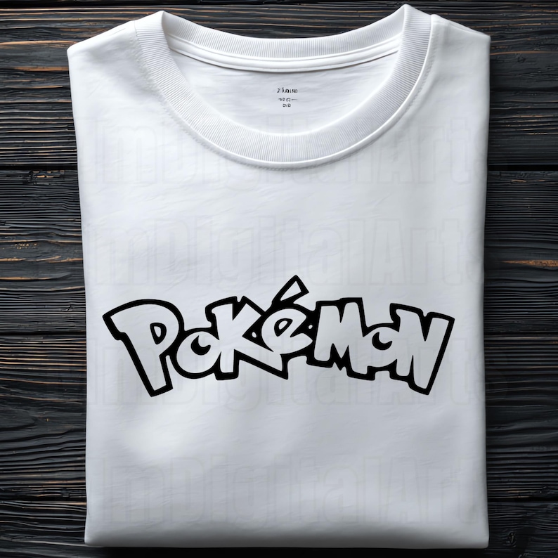 May include: White t-shirt with the word "Pok&eacute;mon" in black, stylized lettering. The shirt has a crew neck and is folded neatly. The background is a dark wood surface.