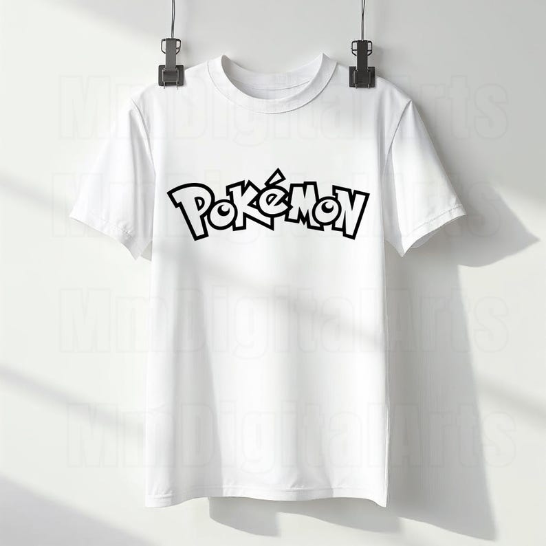 May include: White t-shirt with the word "Pok&eacute;mon" in black, stylized lettering. The shirt is hanging from a metal clip. The shirt has short sleeves and a crew neck.