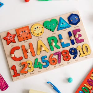 May include: Wooden educational puzzle featuring the name "CHARLIE" in colorful letters and numbers. Includes shapes like stars, squares, circles, hearts, triangles, and hexagons. A fun learning toy for children.