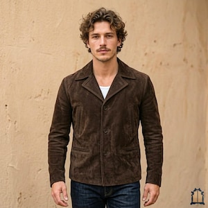 May include: A brown suede jacket with a notched collar and two front pockets. The jacket is buttoned and worn over a white undershirt and blue jeans. The model is standing in front of a beige wall.