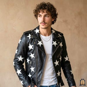 Op de afbeelding: Zwarte leren jas met witte sterrenpatroon. De jas heeft een klassieke biker-stijl met een reverskraag, asymmetrische rits en meerdere zakken. De witte sterren zijn gelijkmatig over de jas verdeeld.