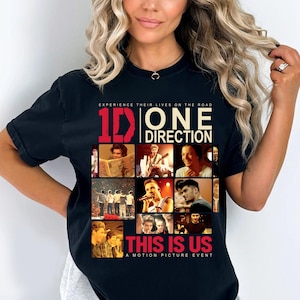 以下が含まれることがあります： 黒いTシャツ。画像とテキストのコラージュ。テキストは赤と白で「1D ONE DIRECTION」と書かれており、その下に「THIS IS US」という言葉があります。シャツには「EXPERIENCE THEIR LIVES ON THE ROAD」と「A MOTION PICTURE EVENT」というフレーズも含まれています。