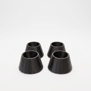 Puede incluir: Cuatro objetos negros en forma de cono con una textura acanalada están dispuestos sobre un fondo blanco. Los objetos tienen una base ancha que se estrecha hacia una abertura más pequeña en la parte superior. Parecen estar hechos de un material mate.