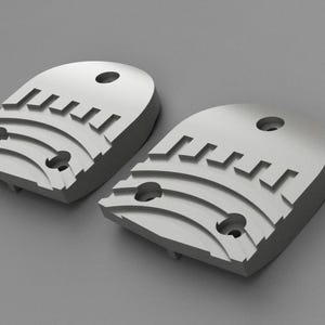 Puede incluir: Dos objetos semicirculares de color gris claro con una serie de ranuras curvas y recortes rectangulares. Cada objeto tiene un agujero circular en la parte superior y dos agujeros más pequeños. Los objetos están sobre un fondo gris.