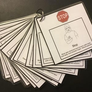 May include: A set of flashcards held together by a metal ring. Each card has black text and illustrations on a white background. The top card reads "STOP" with a hand gesture illustration. Other cards show instructions for various actions.