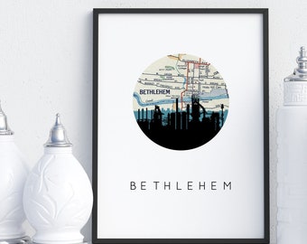 May include: A framed print with a black border featuring a circular map of Bethlehem, Pennsylvania, with a black silhouette of the city's industrial skyline at the bottom. The word "BETHLEHEM" is printed in a simple font below the map. Decorative white vases with silver tops are on either side.
