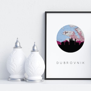 May include: A black framed print with a white background. The print features a circle with a map of Dubrovnik, Croatia, in blue and pink. The city skyline is shown in black against a pink background. The text "DUBROVNIK" is printed below the circle.