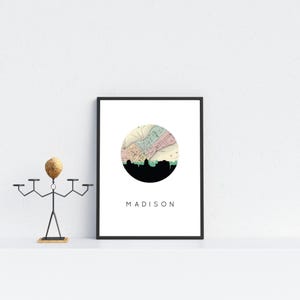 A framed Madison map poster rests on a white shelf next to a metal sculpture with a wooden head.