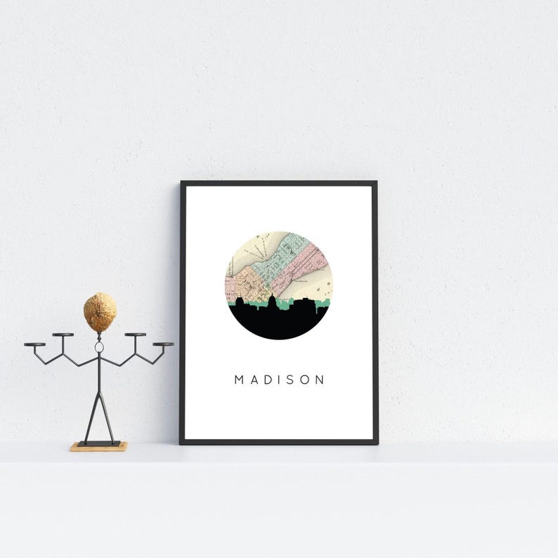 A framed Madison map poster rests on a white shelf next to a metal sculpture with a wooden head.