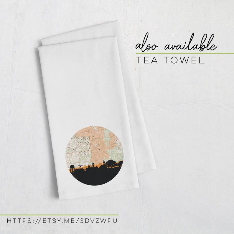 Two folded white tea towels lie on a white surface, with one displaying a circular map and city skyline graphic.