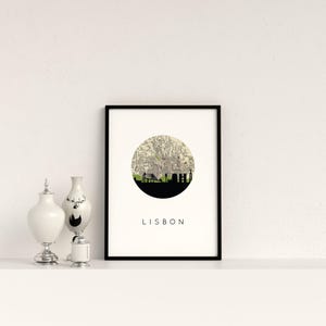Framed Lisbon art print on a shelf alongside decorative silver and white ceramic vessels.