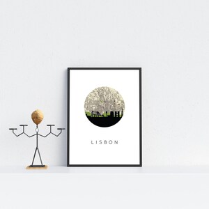Framed Lisbon print resting on a white shelf next to a stylized metal candle holder with a wooden head.