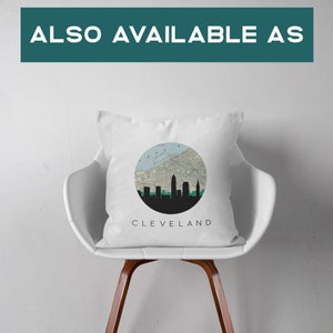 May include: White square pillow with a circular design featuring a map and the silhouette of the Cleveland skyline. The word "CLEVELAND" is printed below the design. The pillow is on a white chair.