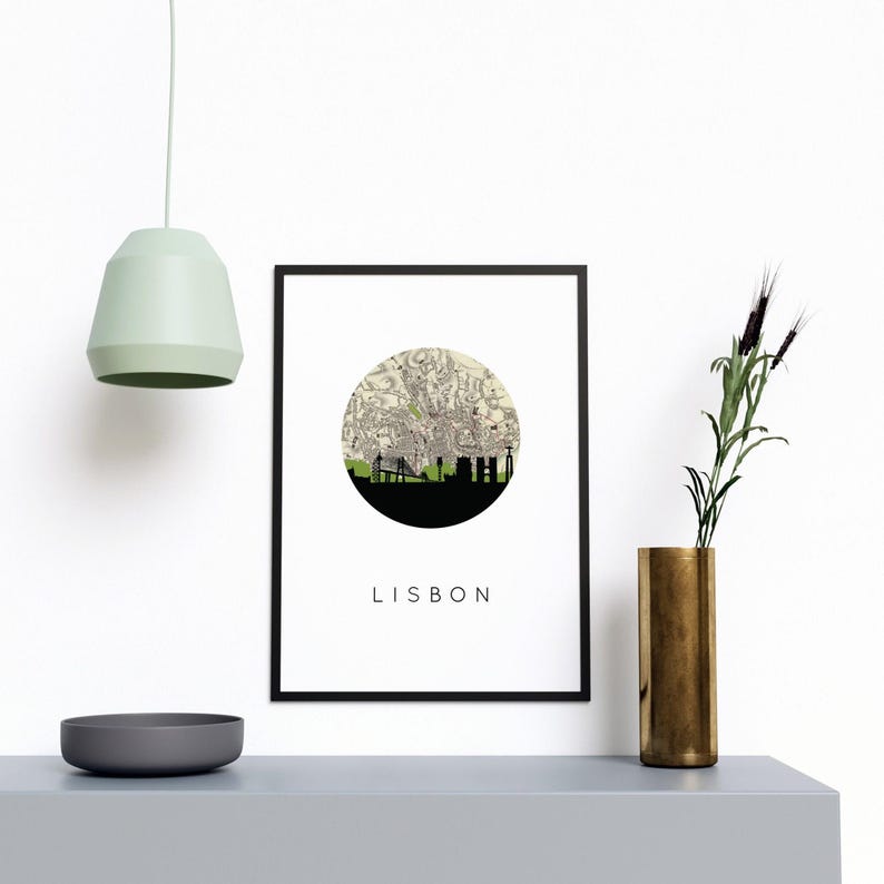 Framed Lisbon print on a gray shelf with a green pendant light, a dark bowl, and a tall gold vase with dried plants.