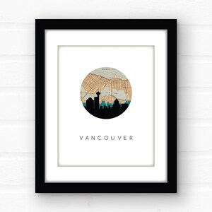 Close-up view of the framed Vancouver art print with a black frame and white mat board, hanging against a white brick wall.