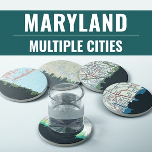May include: Set of five round coasters featuring maps of different cities in Maryland. The coasters are made of cork and have a black backing. The coasters are arranged in a circle on a white surface.