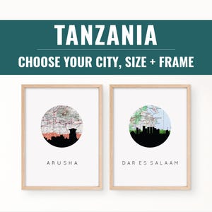 May include: Two framed prints with a map design and city skylines. The top banner reads "TANZANIA" and "CHOOSE YOUR CITY, SIZE + FRAME". One print shows Arusha, the other Dar es Salaam. The frames are light brown.
