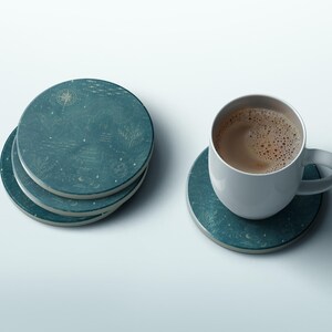 May include: A stack of three round teal coasters featuring gold celestial illustrations of stars and a compass, alongside a single matching coaster topped with a white ceramic mug filled with a brown coffee beverage with visible foam bubbles.