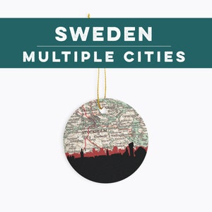 May include: Round ceramic ornament featuring a map of Sweden with the text "SWEDEN MULTIPLE CITIES". The bottom half is black with a red skyline silhouette. A gold string is attached for hanging.