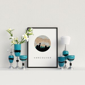 Framed Vancouver map art print on a shelf flanked by vases with white flowers, matching blue and silver candleholders, and a small lamp.
