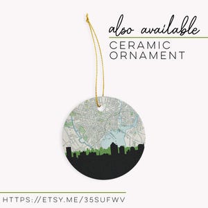 A round ceramic ornament hangs from a gold string, featuring a circular map and city skyline design.