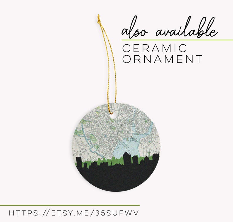 A round ceramic ornament hangs from a gold string, featuring a circular map and city skyline design.